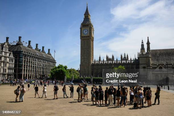 Tourists walk on the sun-baked Parliament Square on July 14, 2022 in London, England. Usually grass-covered, the heat has seen the grass dry and die....