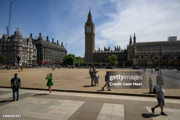 Tourists walk on the sun-baked Parliament Square on July 14, 2022 in London, England. Usually grass-covered, the heat has seen the grass dry and die....