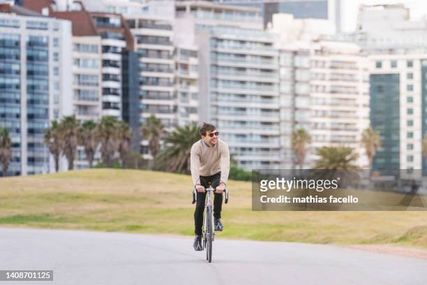 man riding his bike in the city with sunflare on the right - montevideo photos et images de collection