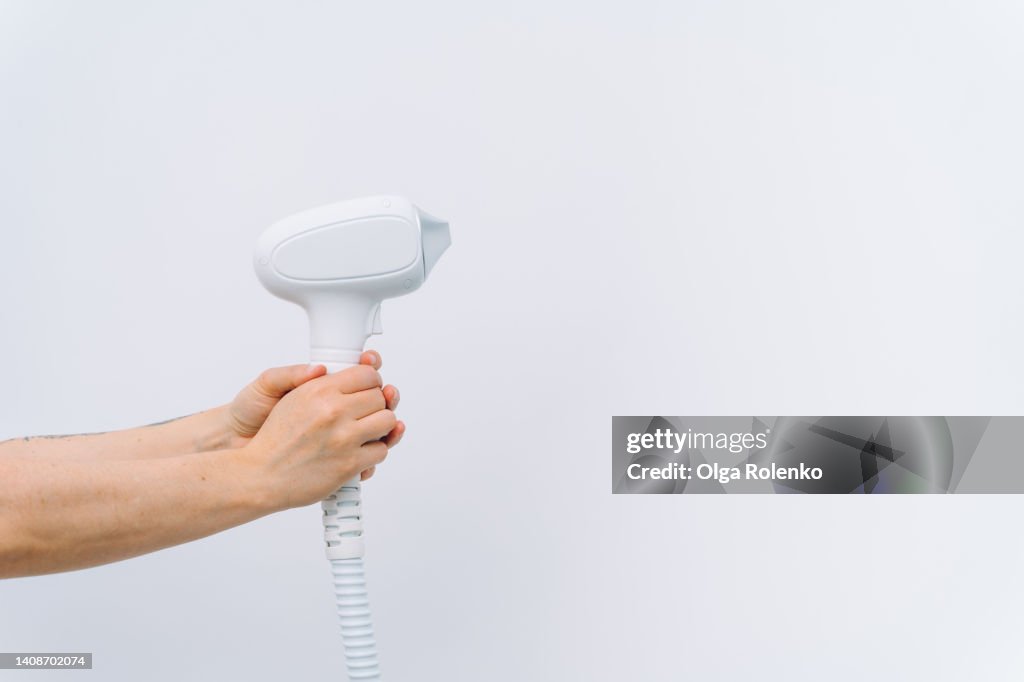 Unrecognizable woman hands holding laser removal handpiece like a gun in white studio