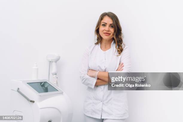 esthetician doctor or medical worker with crossed hands stand near laser hair removal machine on white background - esthetician stock pictures, royalty-free photos & images