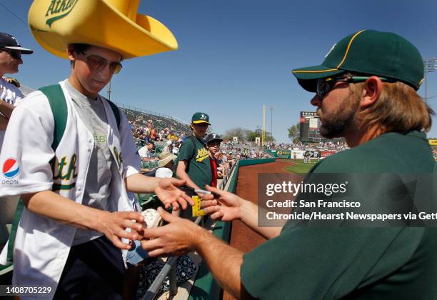 Reliever Andrew Carignan autographs a baseball for A's fan Benjy Egel, of Davis before Oakland's Cactus League spring training game against the...