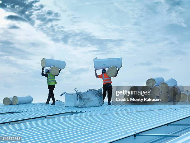 workmen carrying rolls of insulation to install into factory roof - carry foundation stock-fotos und bilder