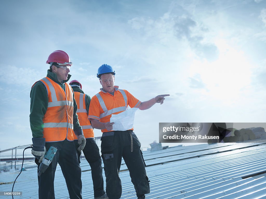 Workman and apprentice discussing plans on factory roof