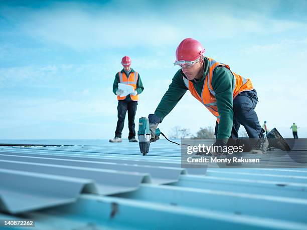 building foreman reading plans as workman insulates factory roof - laborer stock-fotos und bilder