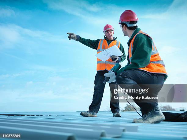 building foreman holding plans and directing apprentice on factory roof - leitwarte stock-fotos und bilder