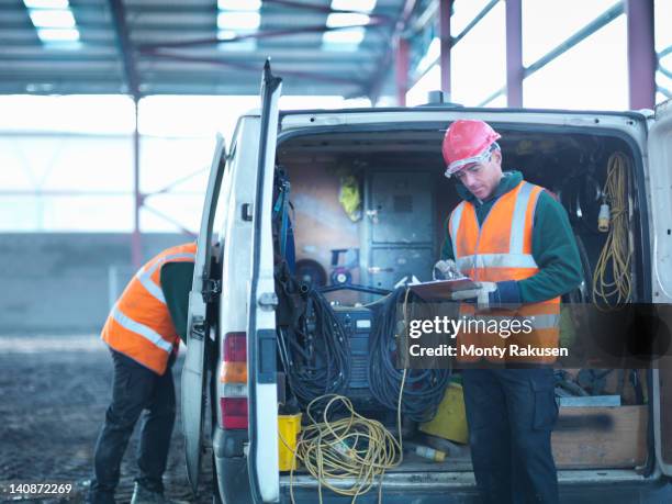 construction worker checking clipboard in back of van on building site - tradesman van stock pictures, royalty-free photos & images