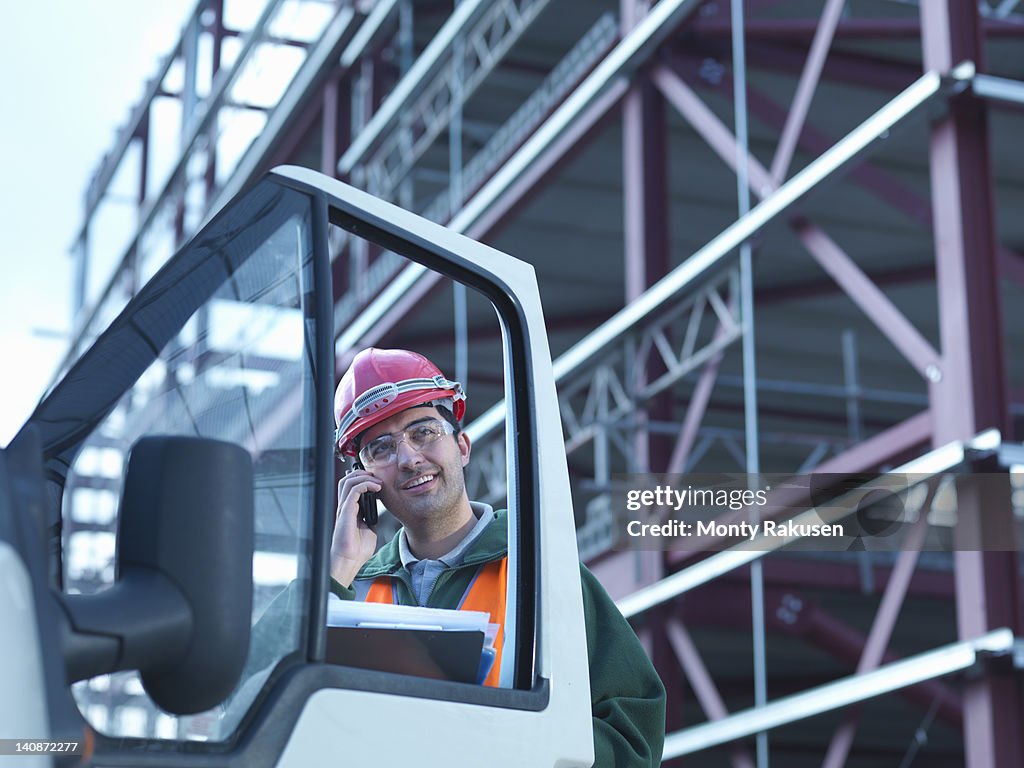 Workman using moble phone by van and steel construction frame on building site