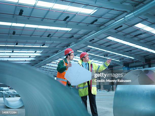 site foreman advising apprentice with plans in partly completed factory - factory blueprint stock pictures, royalty-free photos & images