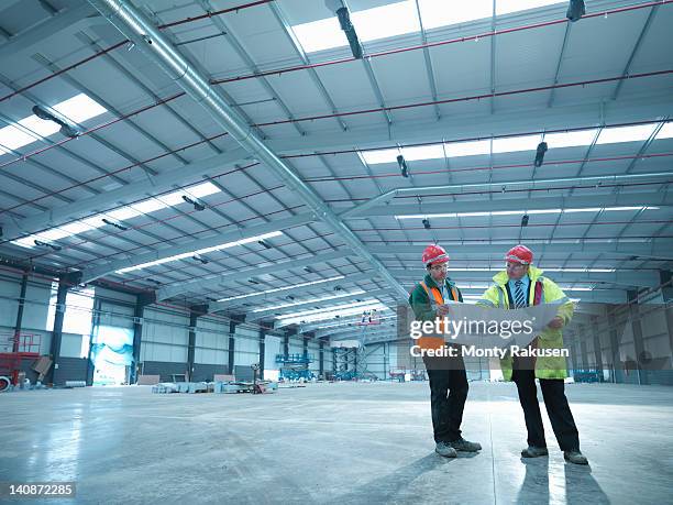 site foreman advising apprentice over plans in partly completed factory - factory blueprint stock pictures, royalty-free photos & images