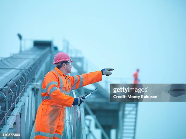 workman in reflective clothing pointing from steps of screening conveyor at quarry - mining low angle foto e immagini stock