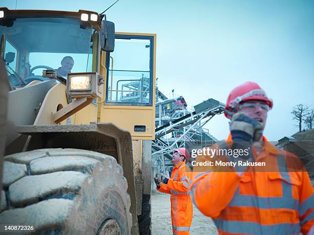 workman using walkie talkie next to industrial digger on quarry site - bulldozer stock-fotos und bilder