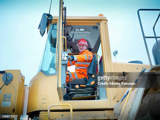 worker driving industrial digger on site - mining low angle foto e immagini stock