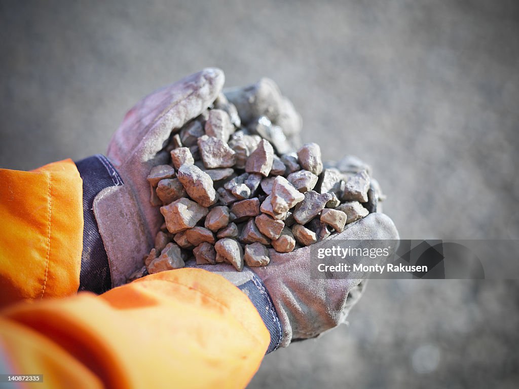 Gloved hands holding crushed stones in quarry site