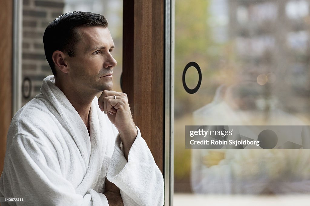 Man in bathrobe looking out window