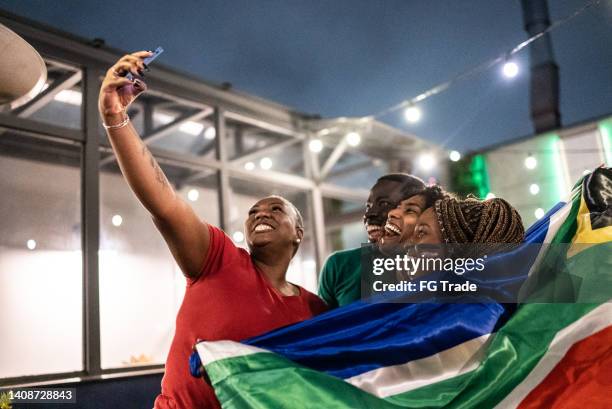 freunde von sportfans, die ein selfie mit einem mobiltelefon in einer bar machen und die südafrikanische flagge halten - traditionelle südafrikanische kultur stock-fotos und bilder