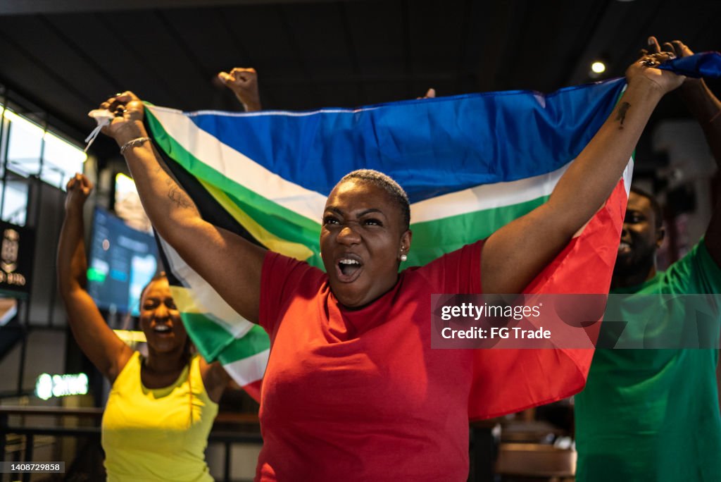 Freunde feiern südafrikanisches Team, das in einer Bar ein Tor schießt