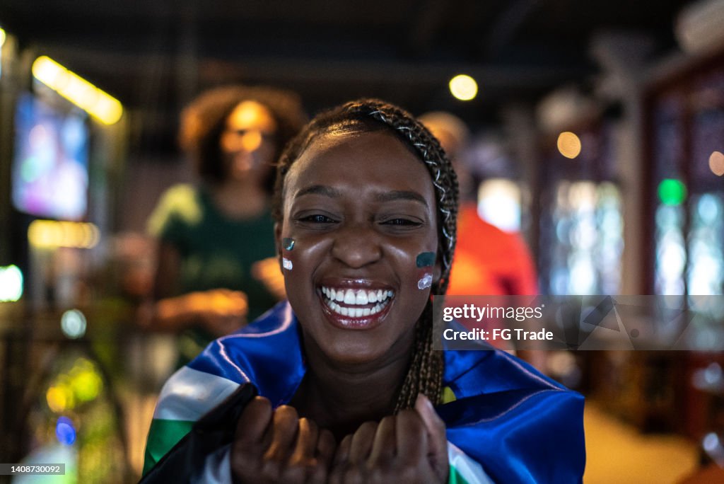 Portrait of a young woman watching game match and celebrating in a bar