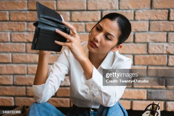 stressed young asian woman sitting and looking at an empty wallet spent all her money on shopping - empty wallet stock-fotos und bilder