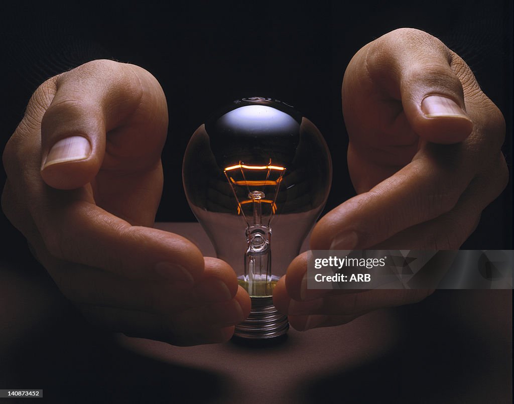 Hands cupping glowing light bulb