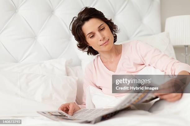 smiling woman reading newspaper in bed - read and newspaper and bed stock pictures, royalty-free photos & images