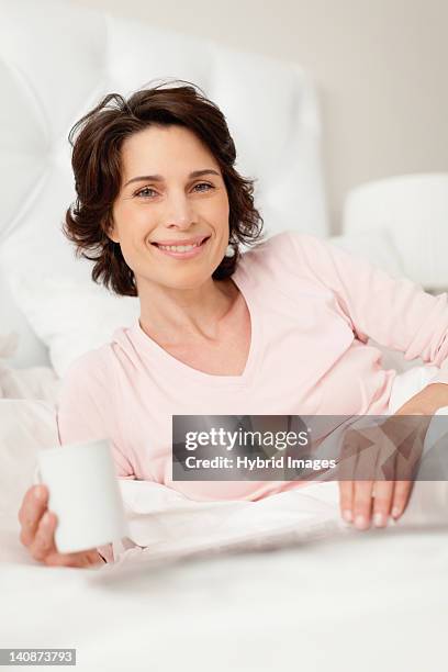 smiling woman reading newspaper in bed - woman short brown hair stock pictures, royalty-free photos & images