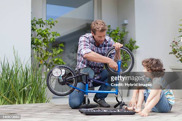 father helping son fix bicycle - fahrrad reparieren stock-fotos und bilder