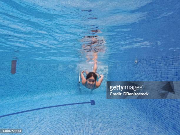 little girl diving into a pool, looking at camera. concept of swimming, diving, summer sport, vacation, recreation and fun. - girl diving fotografías e imágenes de stock