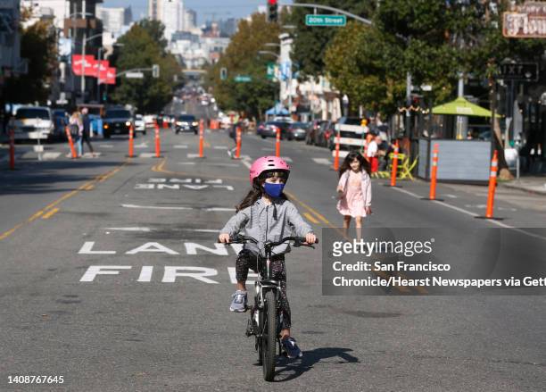 Sofia Manzari peddles and her sister Nina walks down the middle of the 900 block of Valencia Street, which is closed to vehicle traffic on weekends...