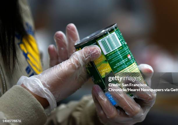Olivia Vera verifies the expiration date on a can of corn while volunteering at the Alameda County Community Food Bank in Oakland, Calif. On...