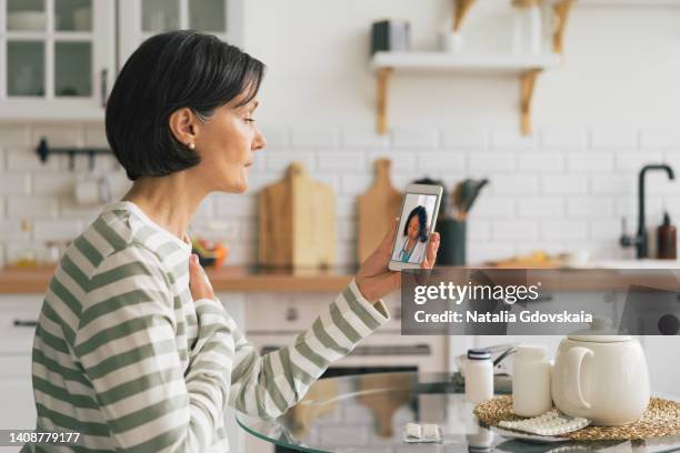 woman calling doctor online on smartphone and telling about chest pain, cough and heartburn. telemedicine concept. future teleconsulting. diagnostic from home. videoconference with therapist. sick female asking for help in kitchen - old cough stock pictures, royalty-free photos & images