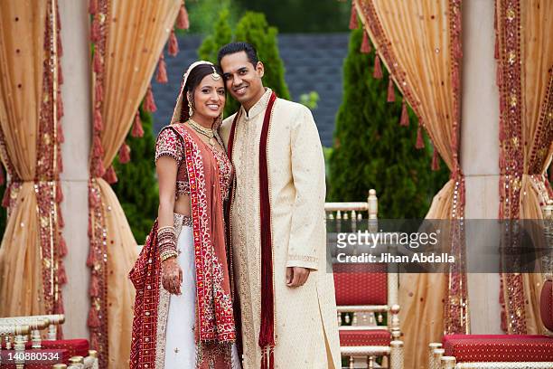 smiling indian couple in traditional wedding clothing - bride and groom looking at camera stock-fotos und bilder