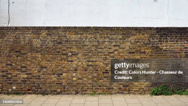 weathered brown brick and white painted cement block walls with empty cement slab pavement in london, england, uk - bakstenen muur stockfoto's en -beelden