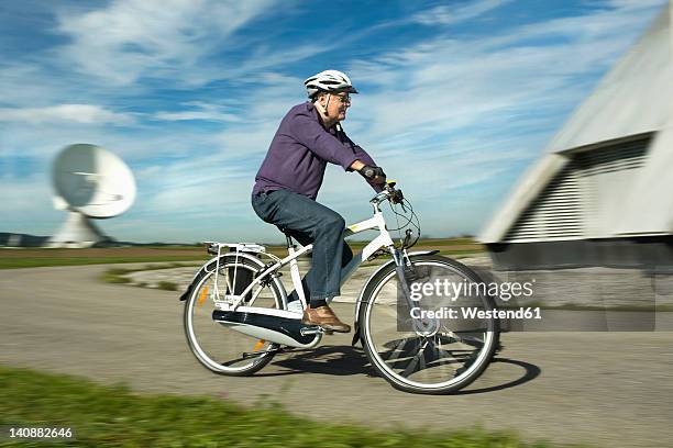 germany, bavaria, raisting, man riding electric bicycle near radio station - ebike stockfoto's en -beelden