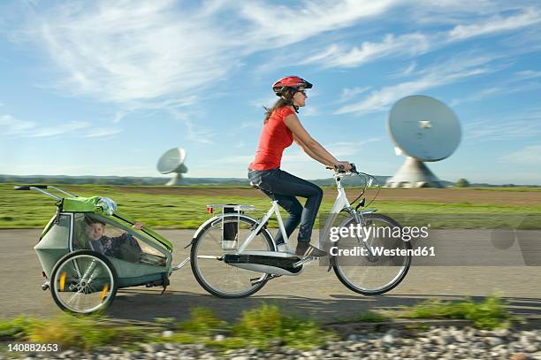 germany, bavaria, raisting, woman with girl riding child trailer near radio station - family riding bikes with helmets stock pictures, royalty-free photos & images