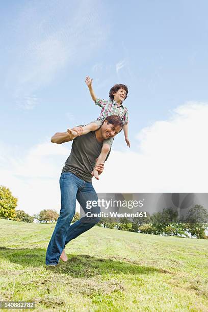 germany, bavaria, father carrying son on shoulder in park, smiling - person auf den schultern tragen stock-fotos und bilder
