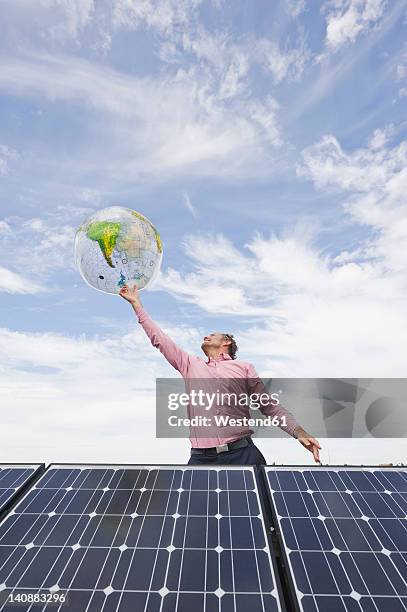 germany, munich, mature man balancing globe on finger in solar plant - world at your fingertips fotografías e imágenes de stock