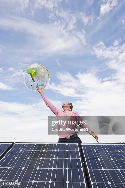 germany, munich, mature man balancing globe on finger in solar plant - world at your fingertips stockfoto's en -beelden
