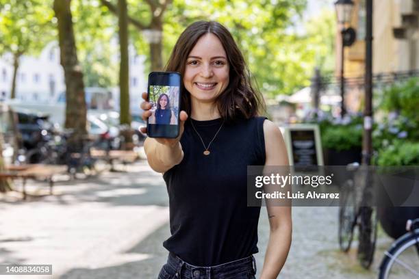 happy young woman showing her photo on her phone while standing outdoors. - demonstration photos et images de collection