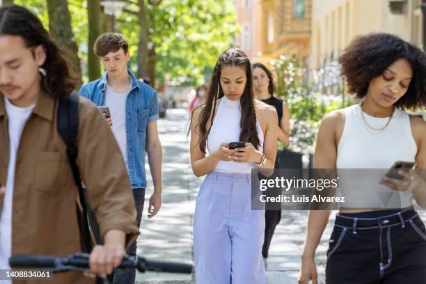 multiracial people walking down the street using their mobile phones - beroende bildbanksfoton och bilder
