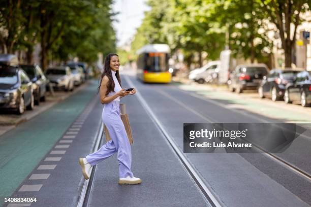 young woman crossing the street with mobile phone. - sleeveless ストックフォトと画像