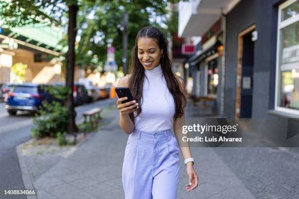 african young woman using her mobile phone on city street - purple trousers stock pictures, royalty-free photos & images