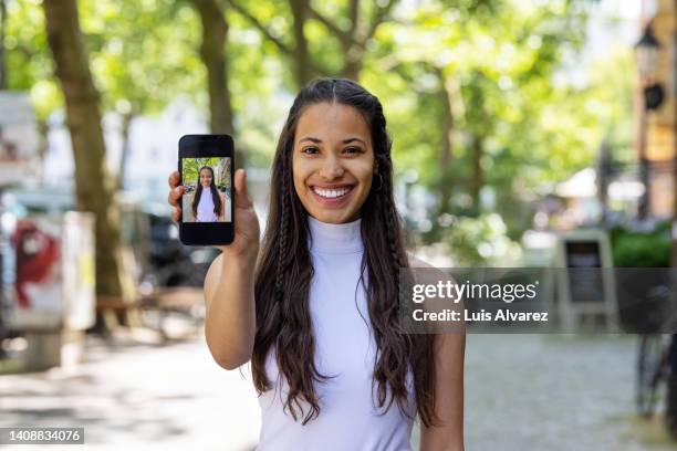 young african woman showing her photo on her phone - presenteren stockfoto's en -beelden