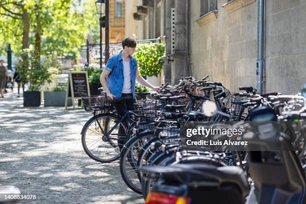 young man parking his bicycle in cycle stand along the street - bicycle parking station stock pictures, royalty-free photos & images