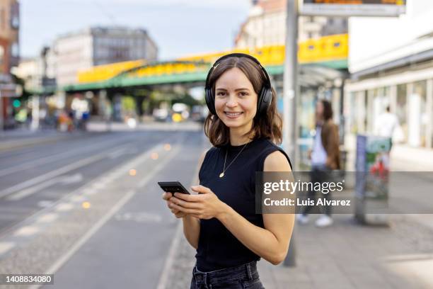 portrait of a happy woman with headphones and mobile phone standing by the city street - berlin people ストックフォトと画像