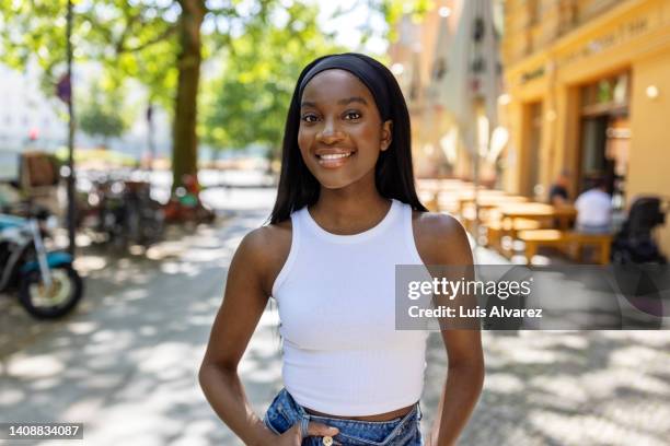 portrait of a beautiful woman in casuals standing on sidewalk and smiling - sleeveless top stock pictures, royalty-free photos & images