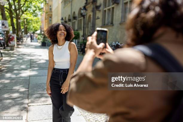 african woman being photographed by her boyfriend on city street - holing iphone stock pictures, royalty-free photos & images