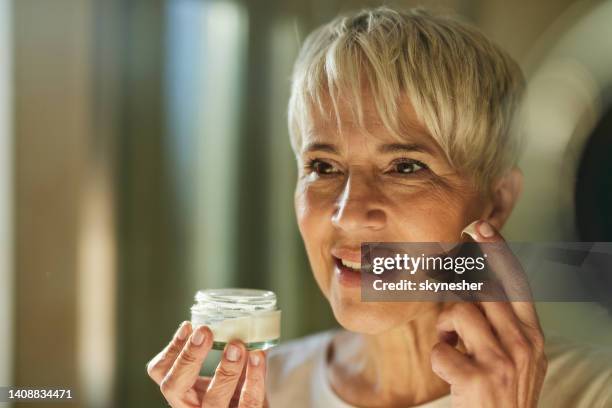 reflection in a mirror of happy senior woman applying anti aging cream. - face cream stock pictures, royalty-free photos & images