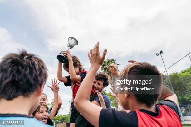 group of kids celebrating together with the coach the winning of a competition on a soccer field - the championship football league stock pictures, royalty-free photos & images