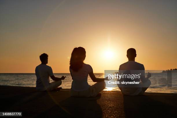 vue arrière de personnes athlétiques méditant sur la plage au coucher du soleil. - man doing yoga in the morning photos et images de collection